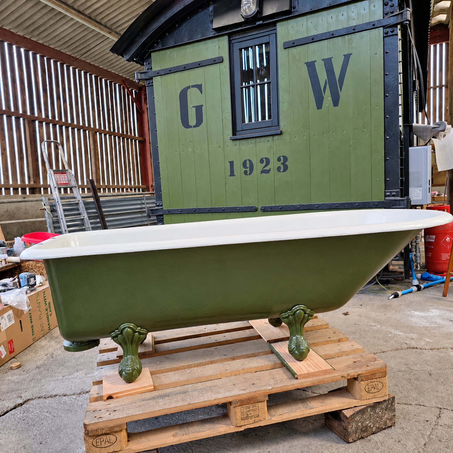 Eine restaurierte grüne freistehende Badewanne auf einer Palette vor dem grünen Wagen