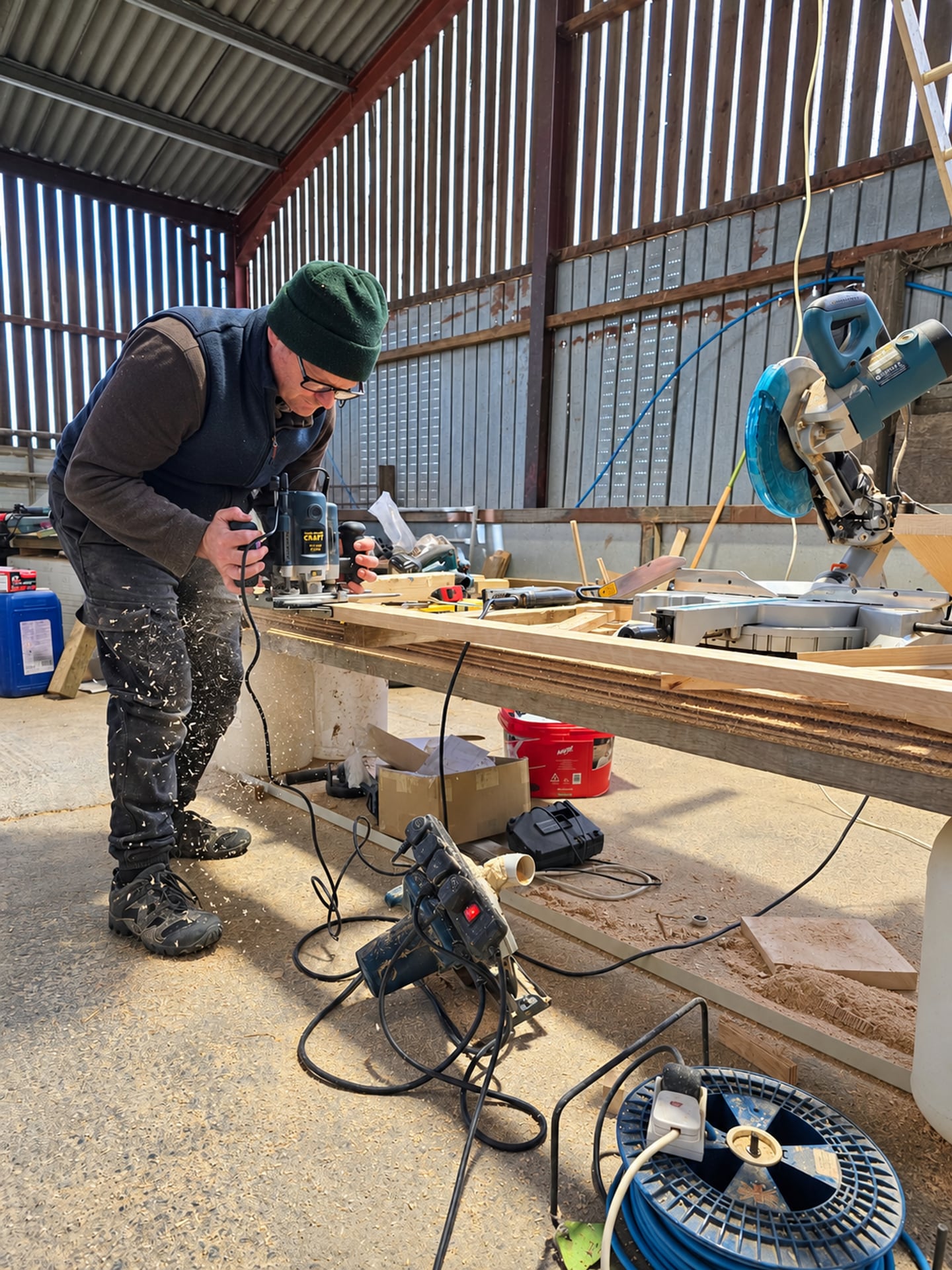 Eine Handwerkerin formt in der Werkstatt mit einer Oberfräse eine Holzplatte